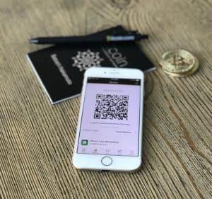 a cell phone screen sits on top of a paper bitcoin booklet. It displays a QR code.